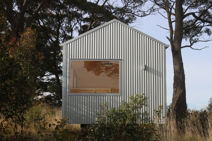 Installed white cabin with a large window between mature trees