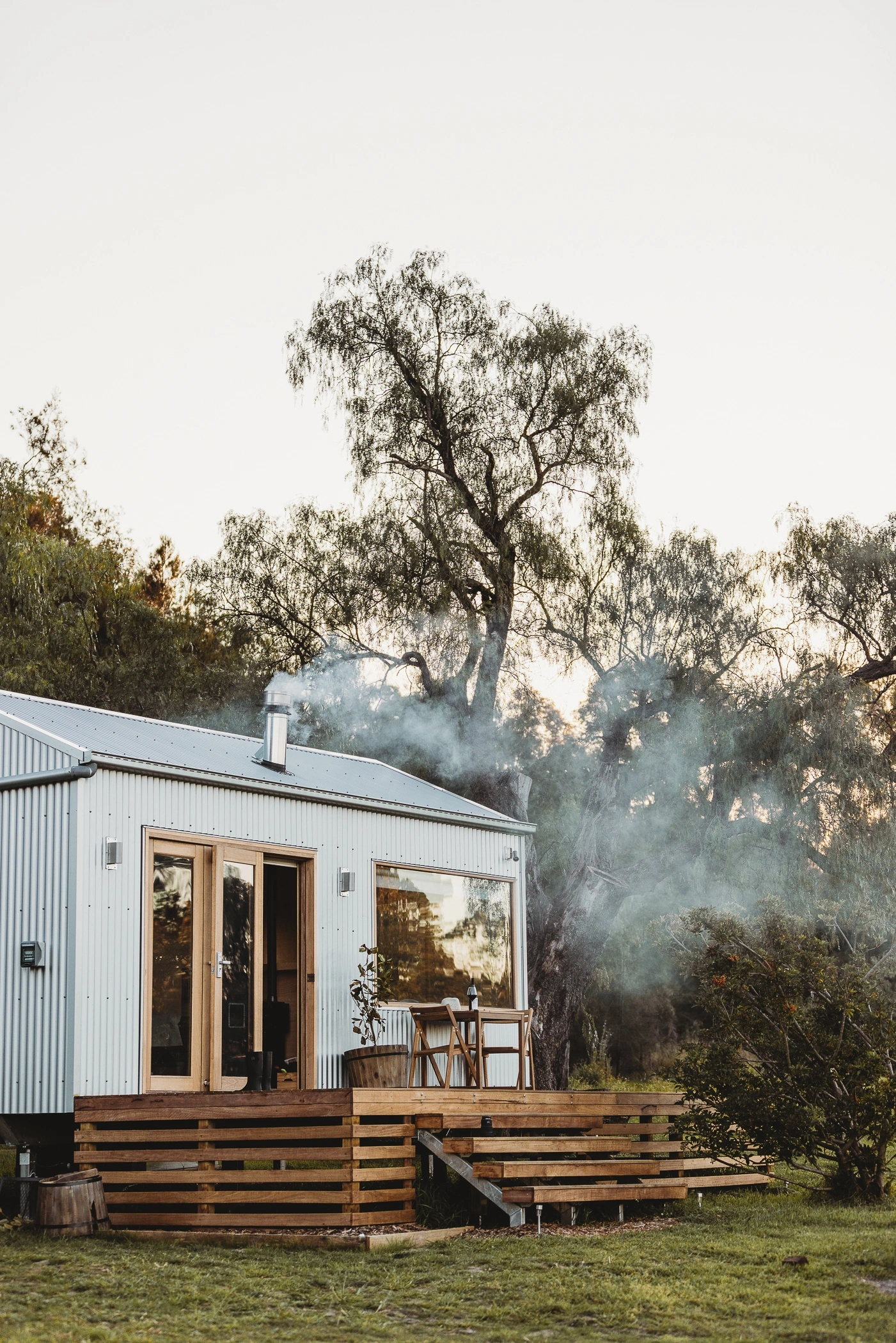 White cabin and deck beneath trees — Zinc Studio Oakvale